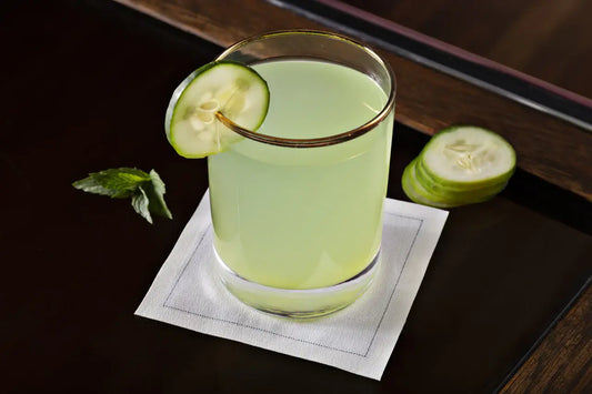 Cocktail glass with cucumber on organic cotton napkin, dark table, cucumber slices nearby