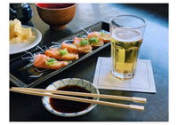 Glass of beer on white organic cotton napkin, sushi and soy sauce at table setting