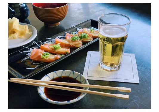 Glass of beer on white organic cotton napkin, sushi and soy sauce at table setting