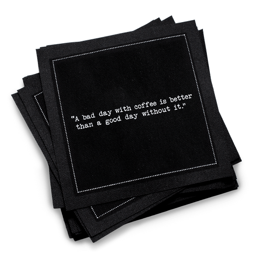 Organic cotton cocktail napkin, black, with white dotted border printed with the quote "A bad day with coffee is better than a good day without it," from Five Star Napkins' Coffee Quotes quote collection