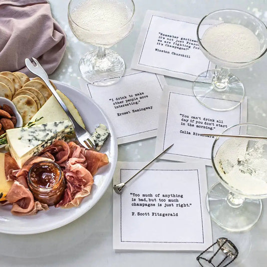 Organic cotton cocktail napkins with printed quotes, champagne glasses, and cheese plate at cocktail party.