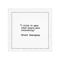 White drinking quote cocktail napkin with black typewriter-style text reading, “I drink to make other people more interesting.” – Ernest Hemingway.