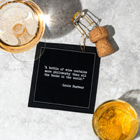 Black cocktail napkin with white typewriter-style text reading, “A bottle of wine contains more philosophy than all the books in the world.” – Louis Pasteur, styled with drinks and a champagne cork.