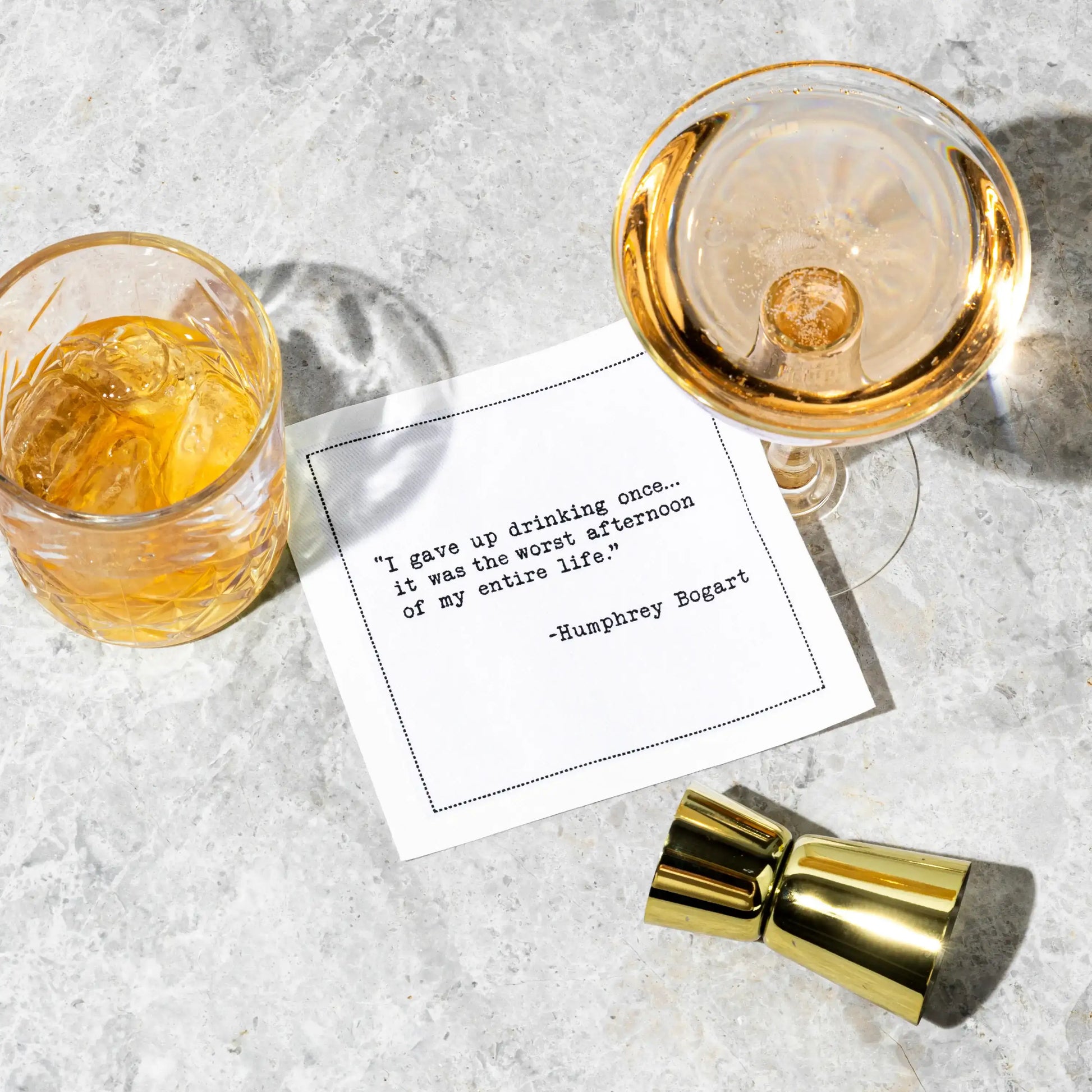 White cocktail napkin with black typewriter-style text reading, “I gave up drinking once... it was the worst afternoon of my entire life.” – Humphrey Bogart, styled between two drinks.