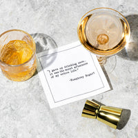 White cocktail napkin with black typewriter-style text reading, “I gave up drinking once... it was the worst afternoon of my entire life.” – Humphrey Bogart, styled between two drinks.