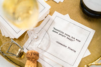 White cocktail napkin with black typewriter-style text reading, “Penicillin cures, but wine makes people happy.” – Alexander Fleming, styled with a wine glass and champagne cork.