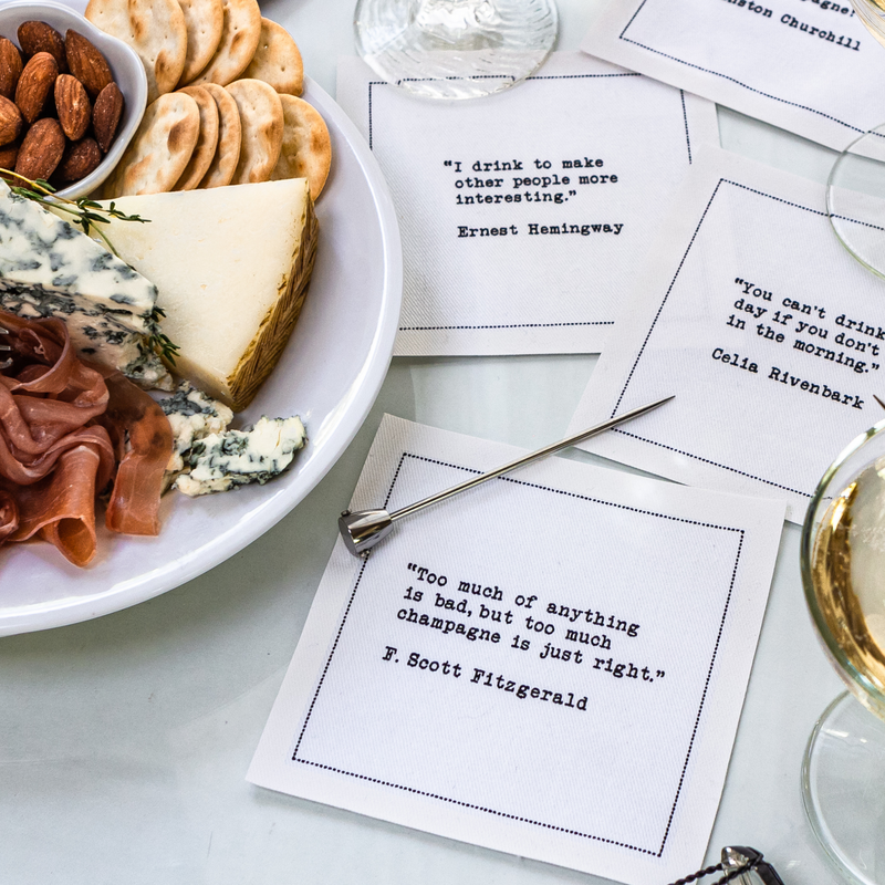 Luxury cocktail napkins with drink quotes next to cheese, crackers, and wine on a table
