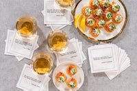 Organic cotton cocktail napkins styled in a flat lay with wine glasses and appetizers, printed with quotes including the Elayne Boosler quote "I've never been married, but I tell people I'm divorced so they won't think something's wrong with me" and the Gerald F. Lieberman quote "Divorce is a declaration of independence with only two signers," from Five Star Napkins' Divorce quote collection