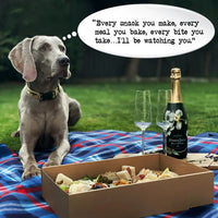 Dog on plaid blanket next to champagne, food box, and two glasses at an outdoor picnic; quote in speech bubble reads, 'Every snack you make, every meal you bake, every bite you take... I'll be watching you.'