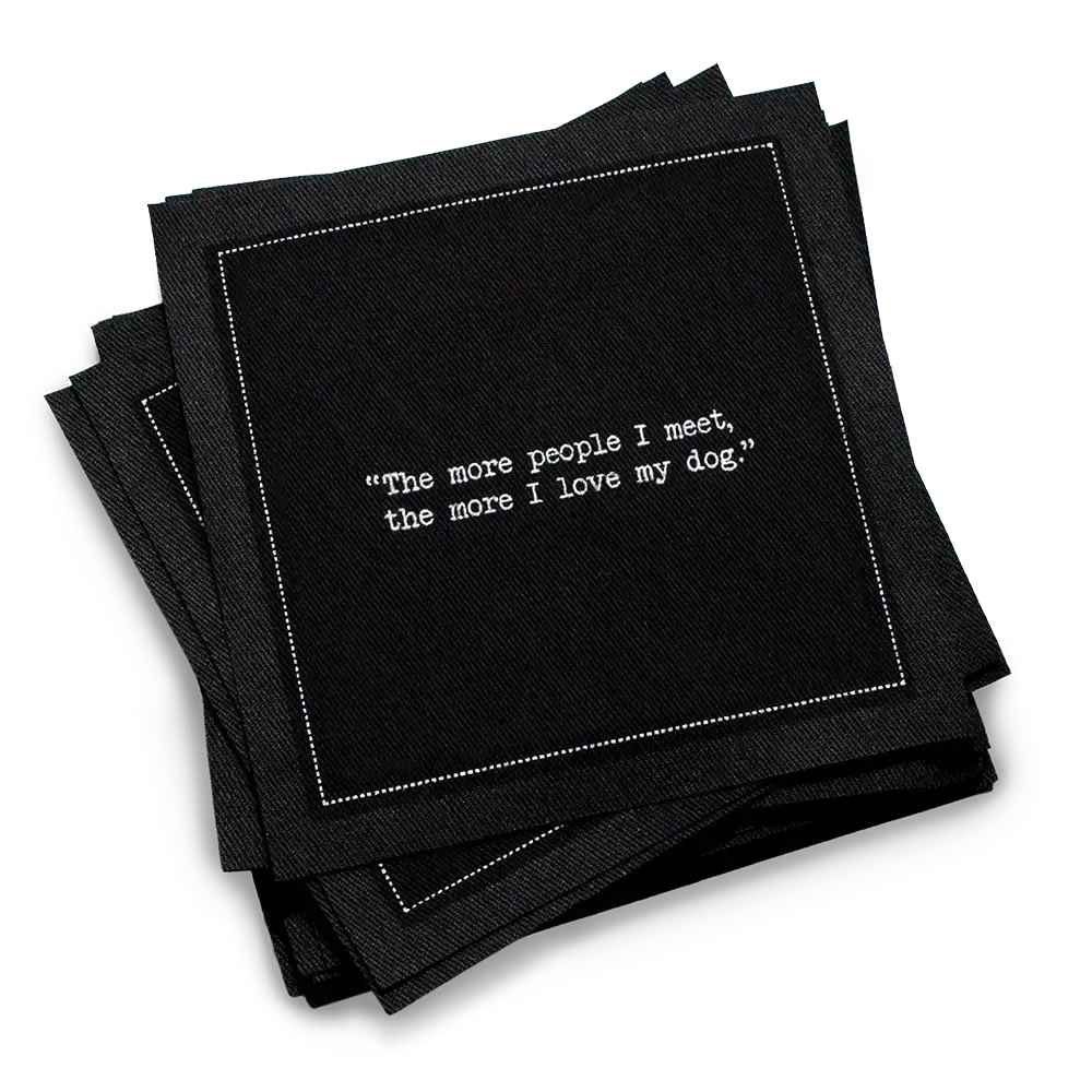 Stack of black organic cotton cocktail napkins with white dotted border printed with the quote “The more people I meet, the more I love my dog,” from Five Star Napkins' Dog quote collection