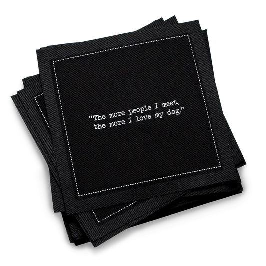 Stack of black organic cotton cocktail napkins with white dotted border printed with the quote “The more people I meet, the more I love my dog,” from Five Star Napkins' Dog quote collection