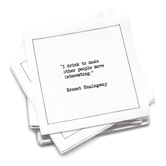 Funny white cotton cocktail napkin from The Drinking Quotes First Edition, printed with black typewriter-style text reading, “I drink to make other people more interesting.” – Ernest Hemingway.
