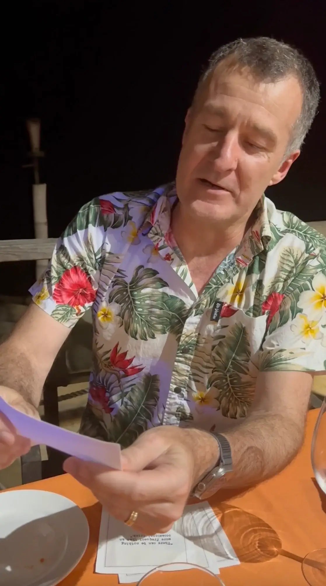 Man at a table holding an organic cotton cocktail napkin from The Drinking Quotes First Edition, with a printed quote visible in a dining setting.