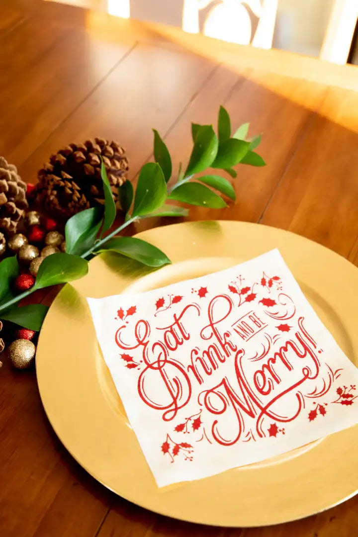 Organic cotton cocktail napkin with red 'Eat Drink and Be Merry' quote on gold plate, holiday table setting