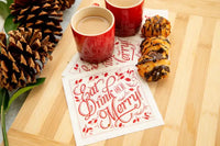 Organic cotton napkin in red print with quote 'Eat, Drink and Be Merry' on a holiday table setting with red mugs and desserts.