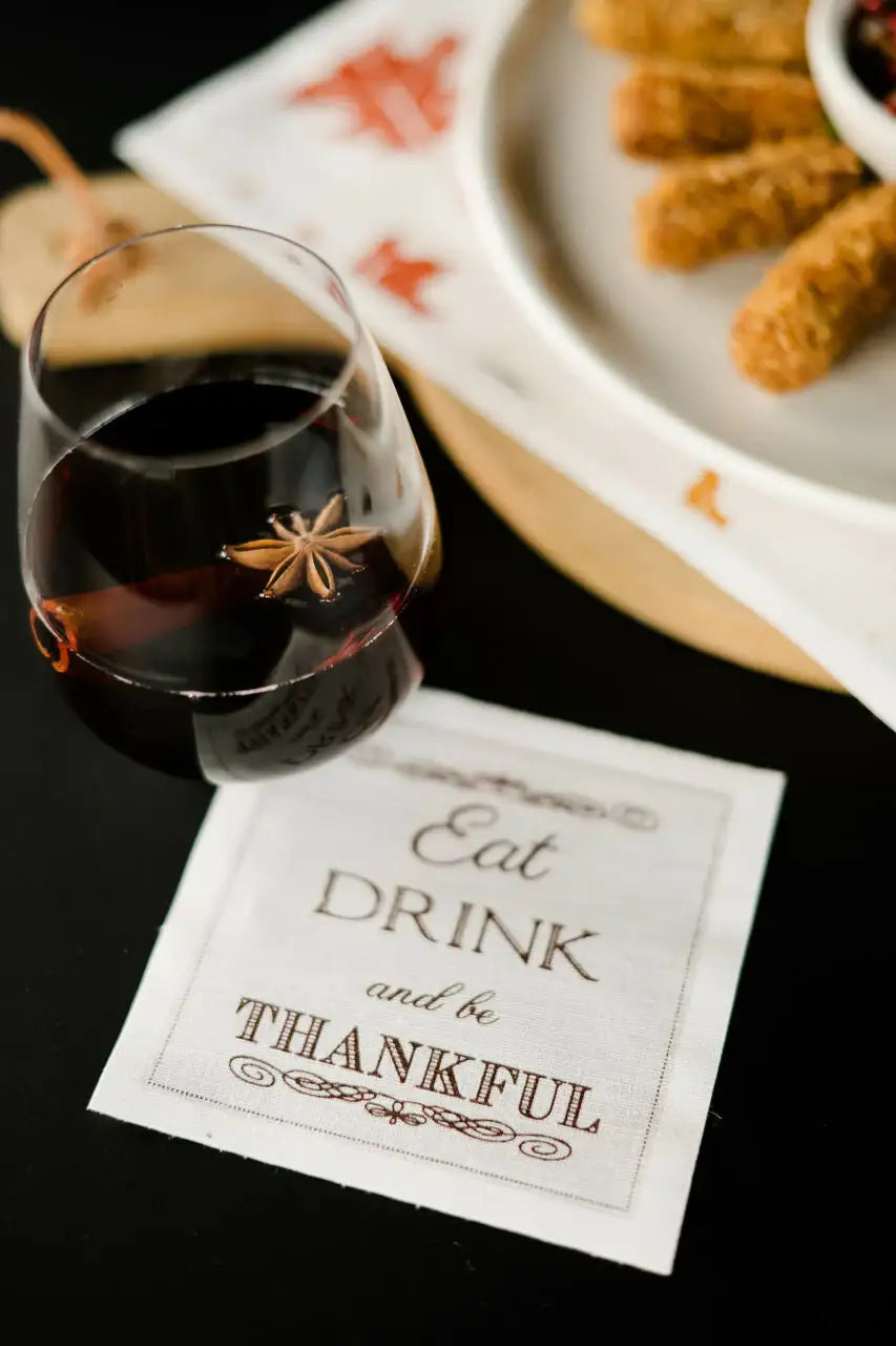 Organic cotton cocktail napkin with 'Eat Drink and be Thankful' quote, styled with wine and appetizers