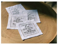 Four organic cotton cocktail napkins with 'Eat, Drink and be Married' quote on a wood table.