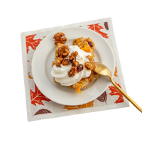 Dessert on a white plate atop a fall-themed luxury cotton cocktail napkin with gold spoon