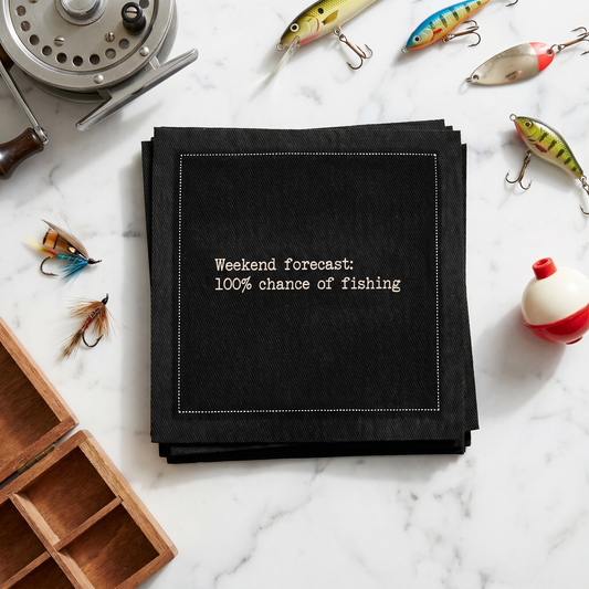 Organic cotton cocktail napkin printed with the quote "Weekend forecast: 100% chance of fishing," styled with fishing lures and tackle on a marble surface, from Five Star Napkins' Fishing Quote collection