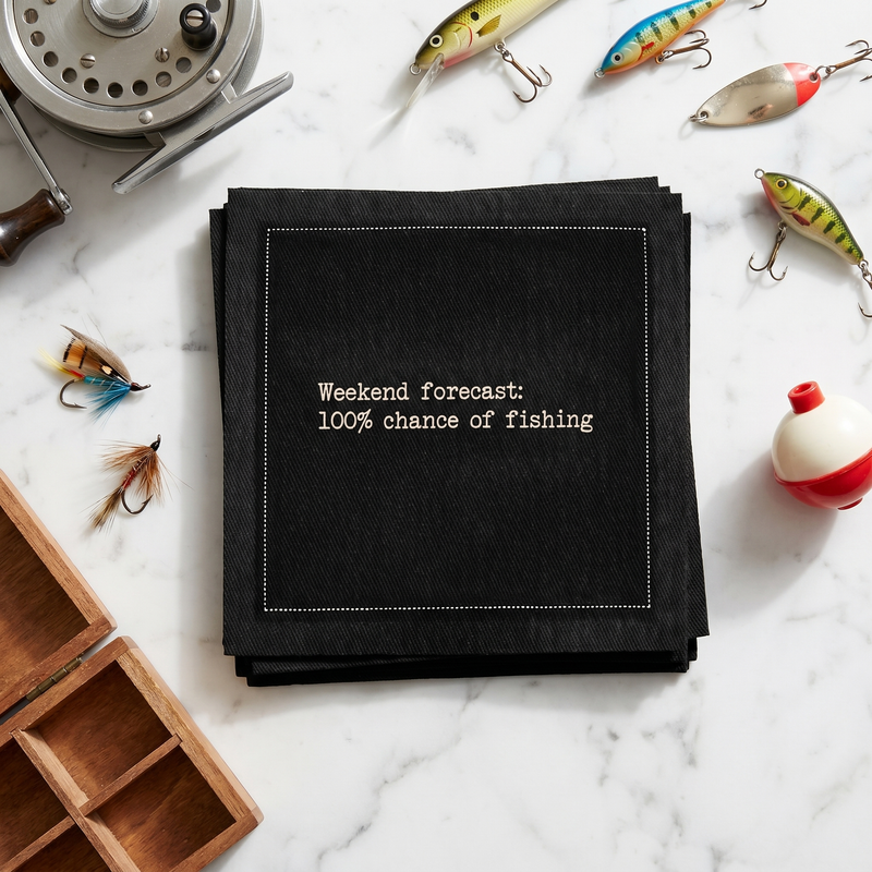 Organic cotton cocktail napkin printed with the quote "Weekend forecast: 100% chance of fishing," styled with fishing lures and tackle on a marble surface, from Five Star Napkins' Fishing Quote collection