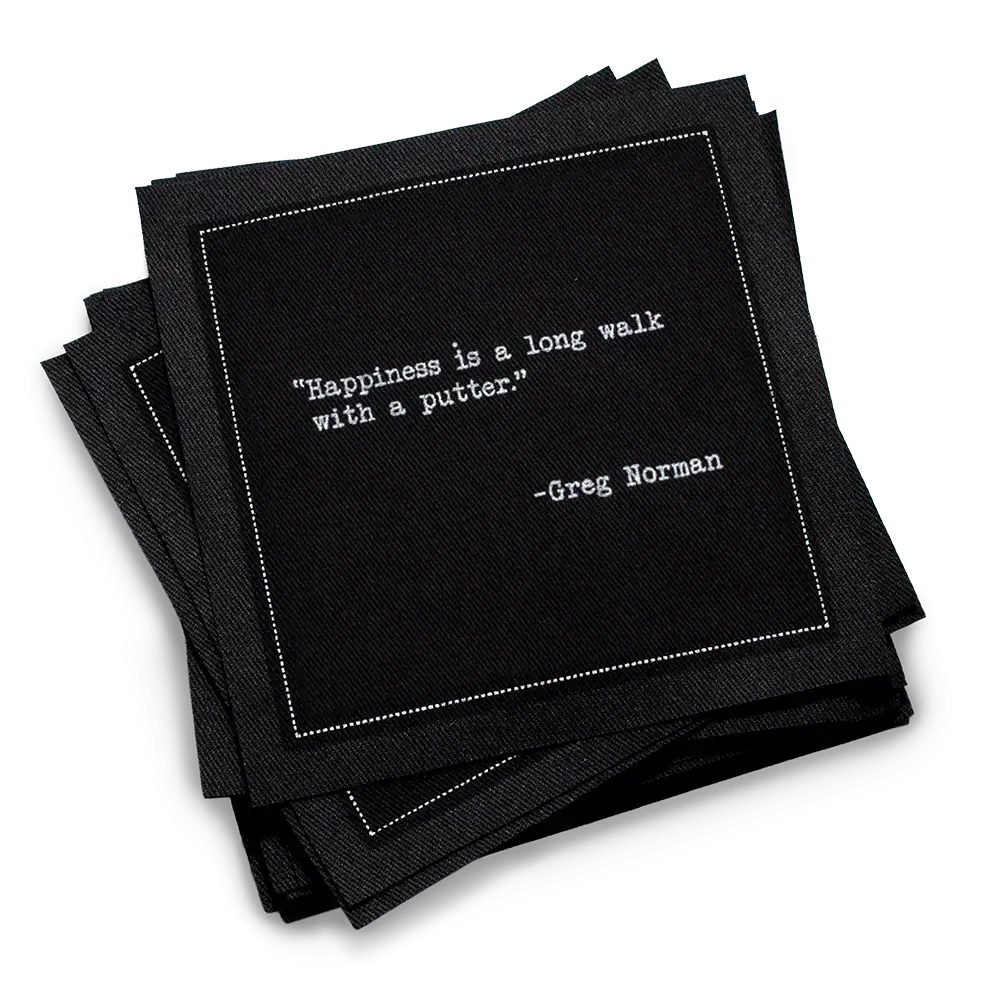 Organic cotton cocktail napkin, black, with white dotted border printed with the Greg Norman quote "Happiness is a long walk with a putter," from Five Star Napkins' Golf Legends quote collection