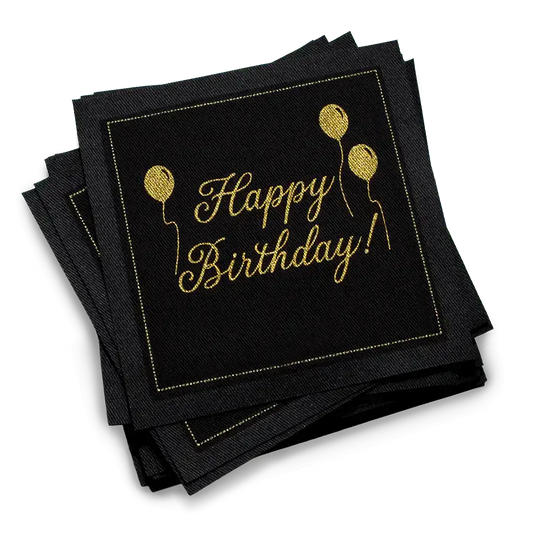 Stack of black organic cotton cocktail napkins with gold “Happy Birthday!” script and balloon design, by Five Star Napkins