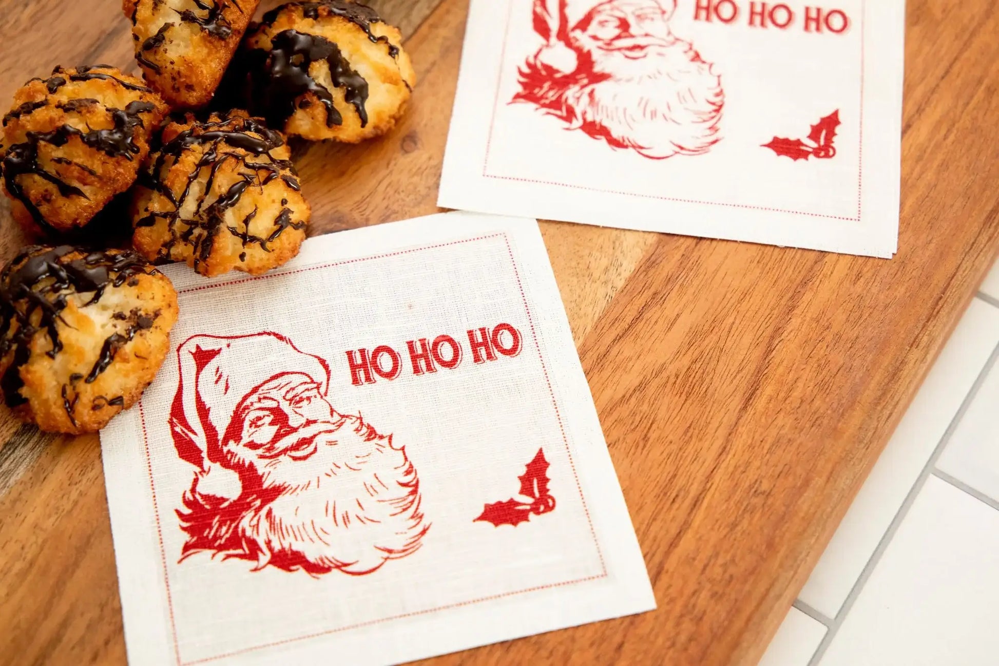 Organic cotton napkin with red Santa illustration and 'HO HO HO' quote, on wooden tray with cookies