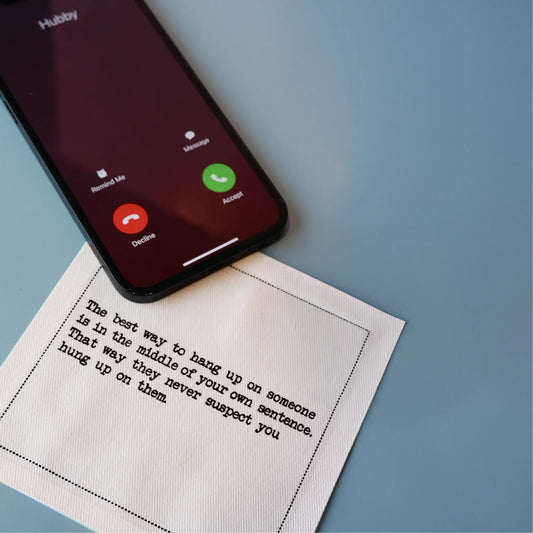 Organic cotton cocktail napkin printed with the quote "The best way to hang up on someone is in the middle of your own sentence. That way they never suspect you hung up on them," styled next to a phone with an incoming call, from Five Star Napkins' Inappropriate Thoughts quote collection