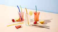 Reusable glass straws styled with iced drinks, lemon, and strawberries, by Five Star Napkins.