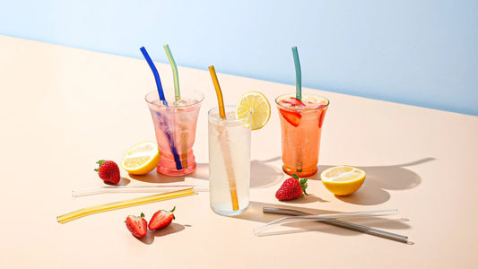 Reusable glass straws styled with iced drinks, lemon, and strawberries, by Five Star Napkins.