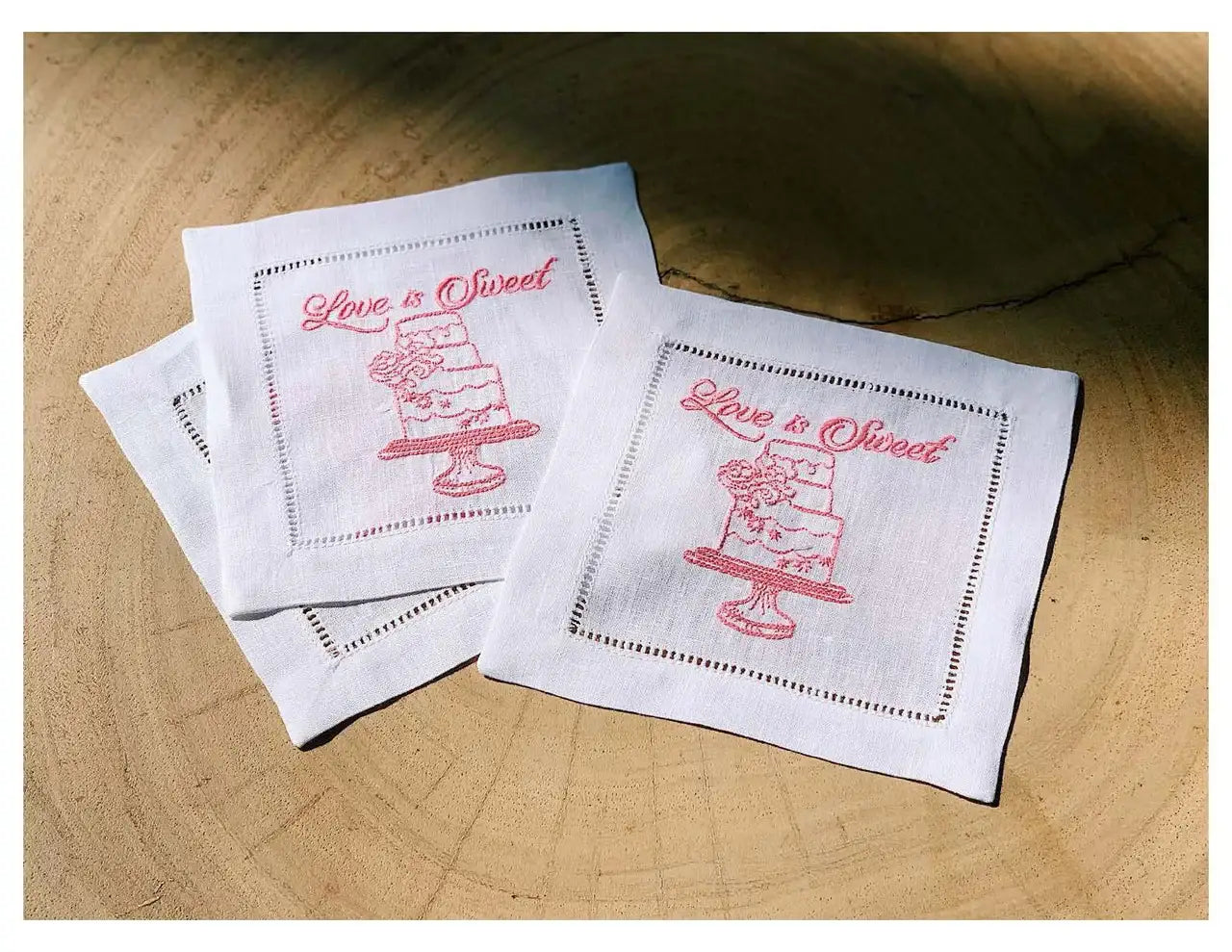 Organic cotton cocktail napkins with pink embroidered 'Love is Sweet' quote and cake design