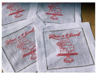 Organic cotton napkins with pink embroidered cake and 'Love is Sweet' quote, styled flat.