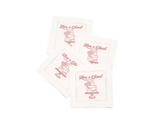 Set of four organic cotton cocktail napkins with 'Love is Sweet' printed quote and cake design.
