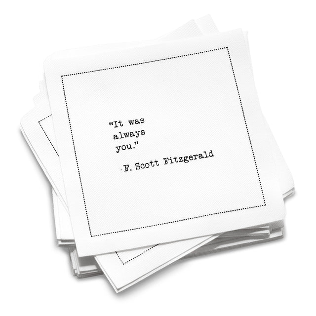 A stack of white Love Quotes cocktail napkins with black dotted borders. The top napkin reads, “It was always you.” —F. Scott Fitzgerald.