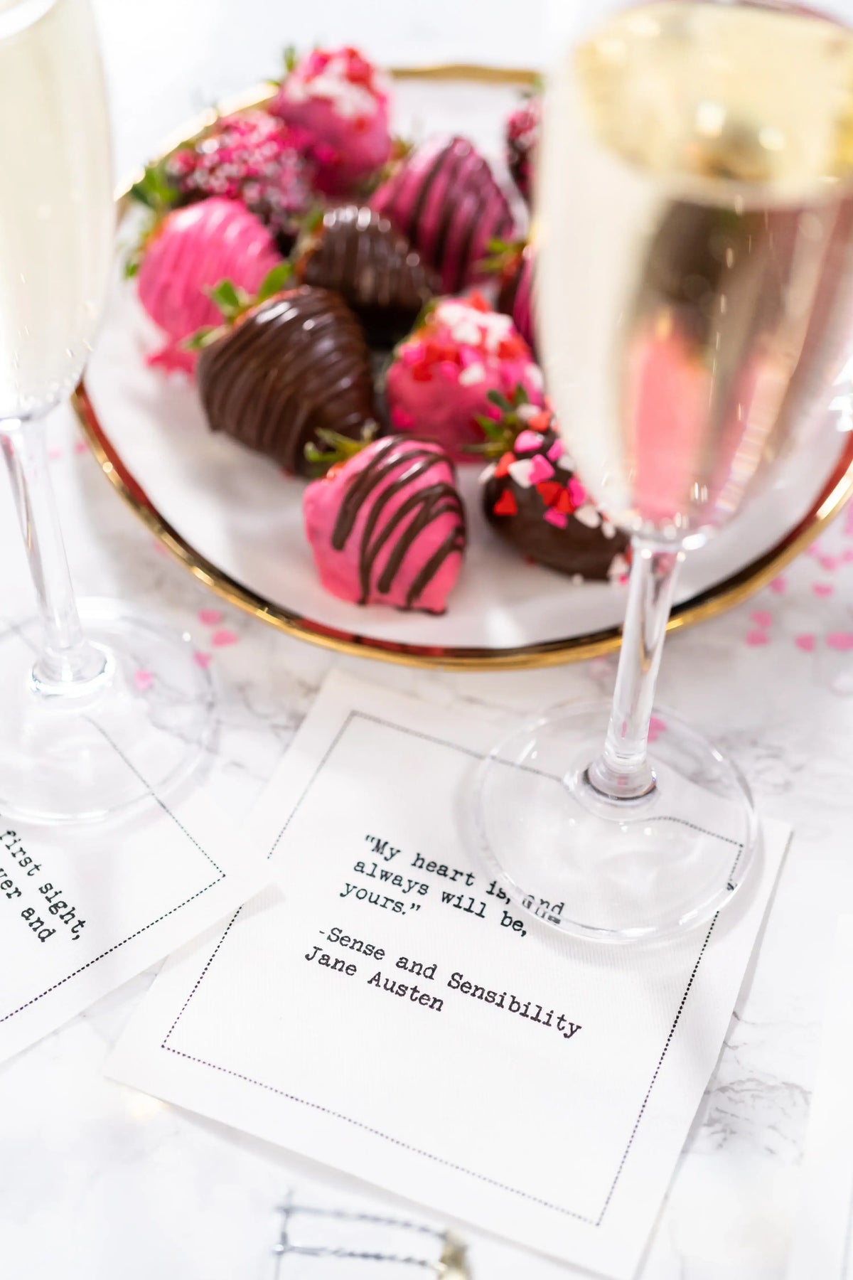 Chocolate-covered strawberries and champagne glasses rest on white Love Quotes cocktail napkins. The featured napkin reads, “My heart is, and always will be, yours.” —Jane Austen, Sense and Sensibility.