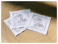 Set of white organic cotton napkins with silver 'Mr. & Mrs.' quote text, stacked on wood surface