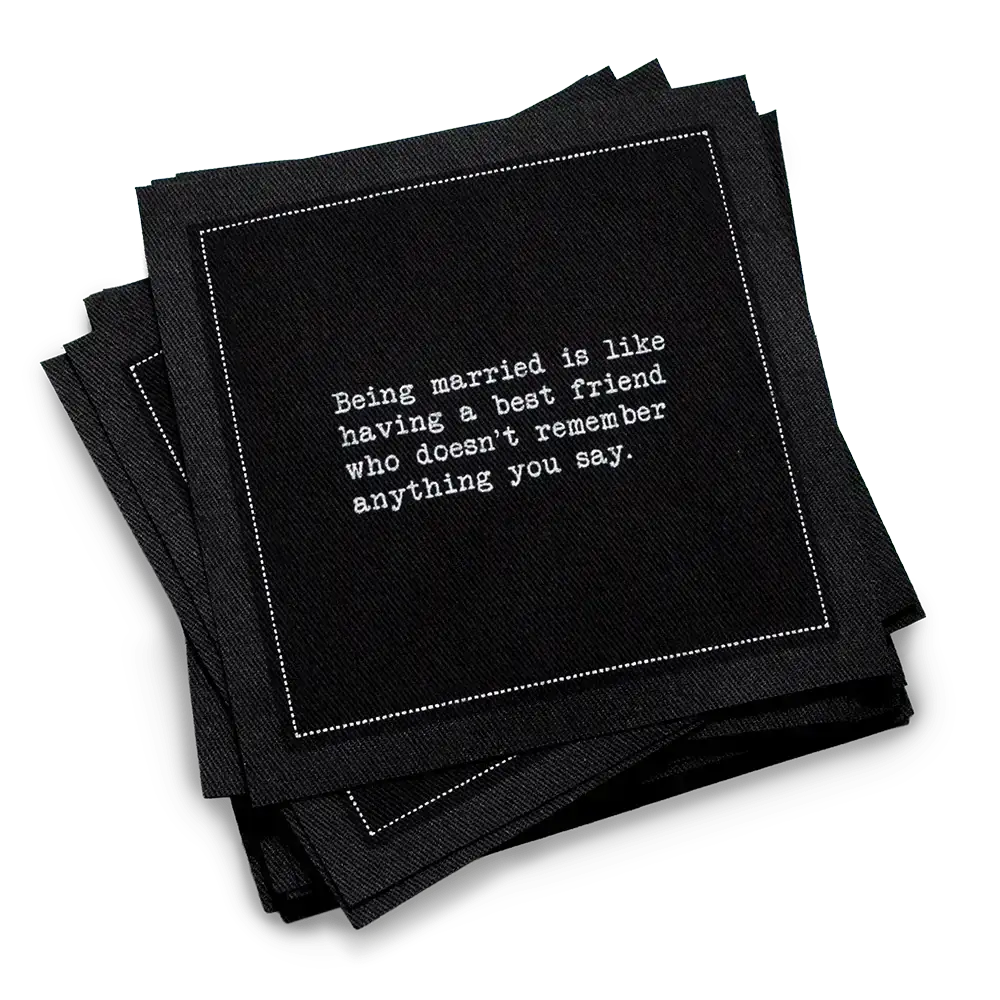 Stack of black marriage quote cocktail napkins with white typewriter-style text reading, “Being married is like having a best friend who doesn’t remember anything you say.”