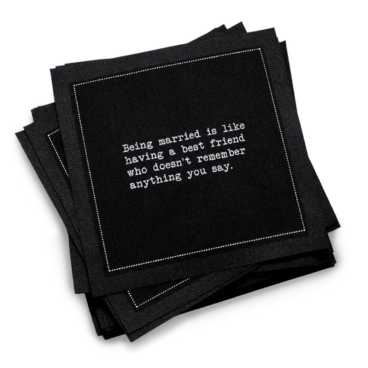 Stack of black marriage quote cocktail napkins with white typewriter-style text reading, “Being married is like having a best friend who doesn’t remember anything you say.”