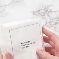 Hand holding a stack of white marriage quote cocktail napkins with black typewriter-style text reading, “Marriage: When dating goes too far.”