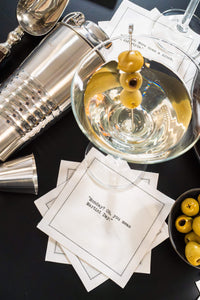 Organic cotton cocktail napkin printed with the quote "Monday? Oh, you mean Martini Day," styled with a martini glass, olives, and a cocktail shaker, from Five Star Napkins' Martini quote collection