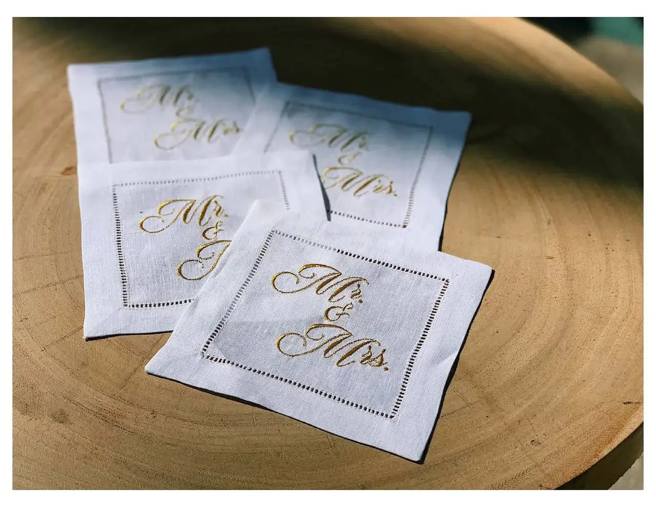 Four organic cotton cocktail napkins embroidered with “Mr. & Mrs.” in gold script, styled on a wood table, by Five Star Napkins.