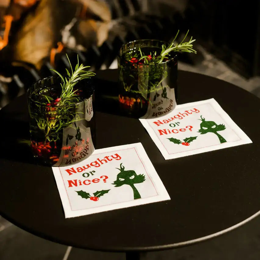 Organic cotton cocktail napkins with 'Naughty or Nice?' quote and holiday drinks on a black table