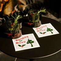Organic cotton cocktail napkins with 'Naughty or Nice?' quote and holiday drinks on a black table