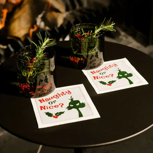 Organic cotton cocktail napkins with 'Naughty or Nice?' quote and holiday drinks on a black table
