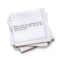 Organic cotton quarter-fold napkin, white, with black dotted border printed with the quote "When you're 60, getting lucky means finding your car in the parking lot," from Five Star Napkins' 60th birthday quote collection