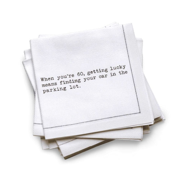 Organic cotton quarter-fold napkin, white, with black dotted border printed with the quote "When you're 60, getting lucky means finding your car in the parking lot," from Five Star Napkins' 60th birthday quote collection