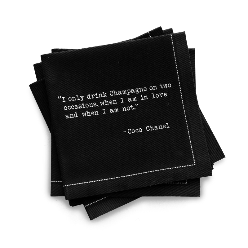 Quarter-fold organic cotton cocktail napkin, black, with white dotted border printed with the Coco Chanel quote "I only drink Champagne on two occasions, when I am in love and when I am not," from Five Star Napkins' Champagne quote collection