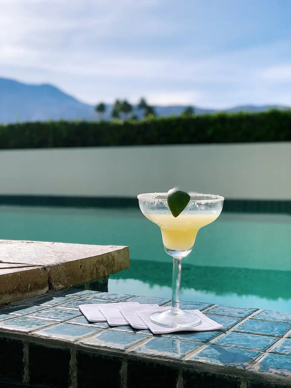 Organic cotton cocktail napkins on tile by a pool with margarita glass and lime wedge