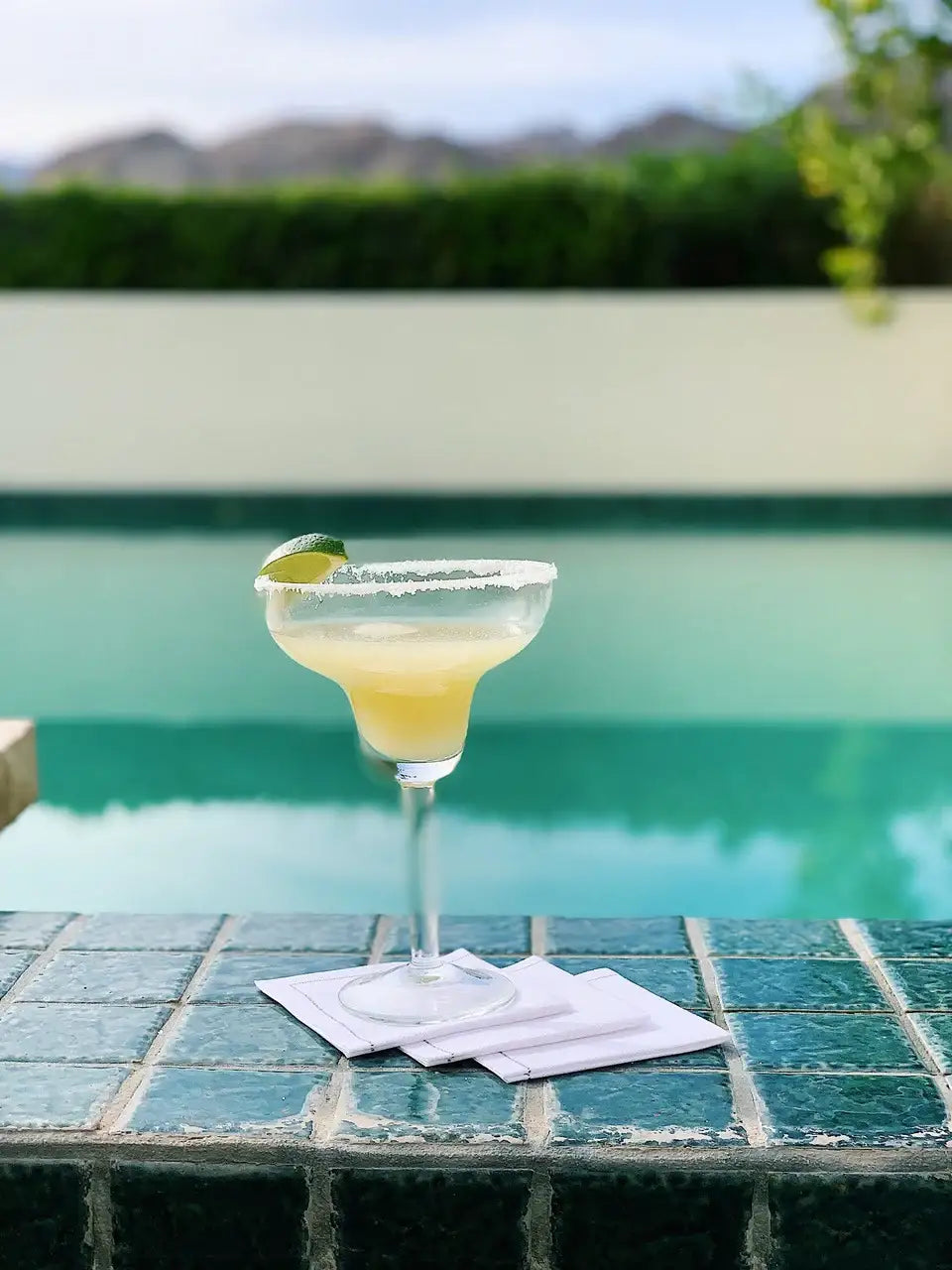 Margarita glass with lime on white organic cotton cocktail napkins by a poolside