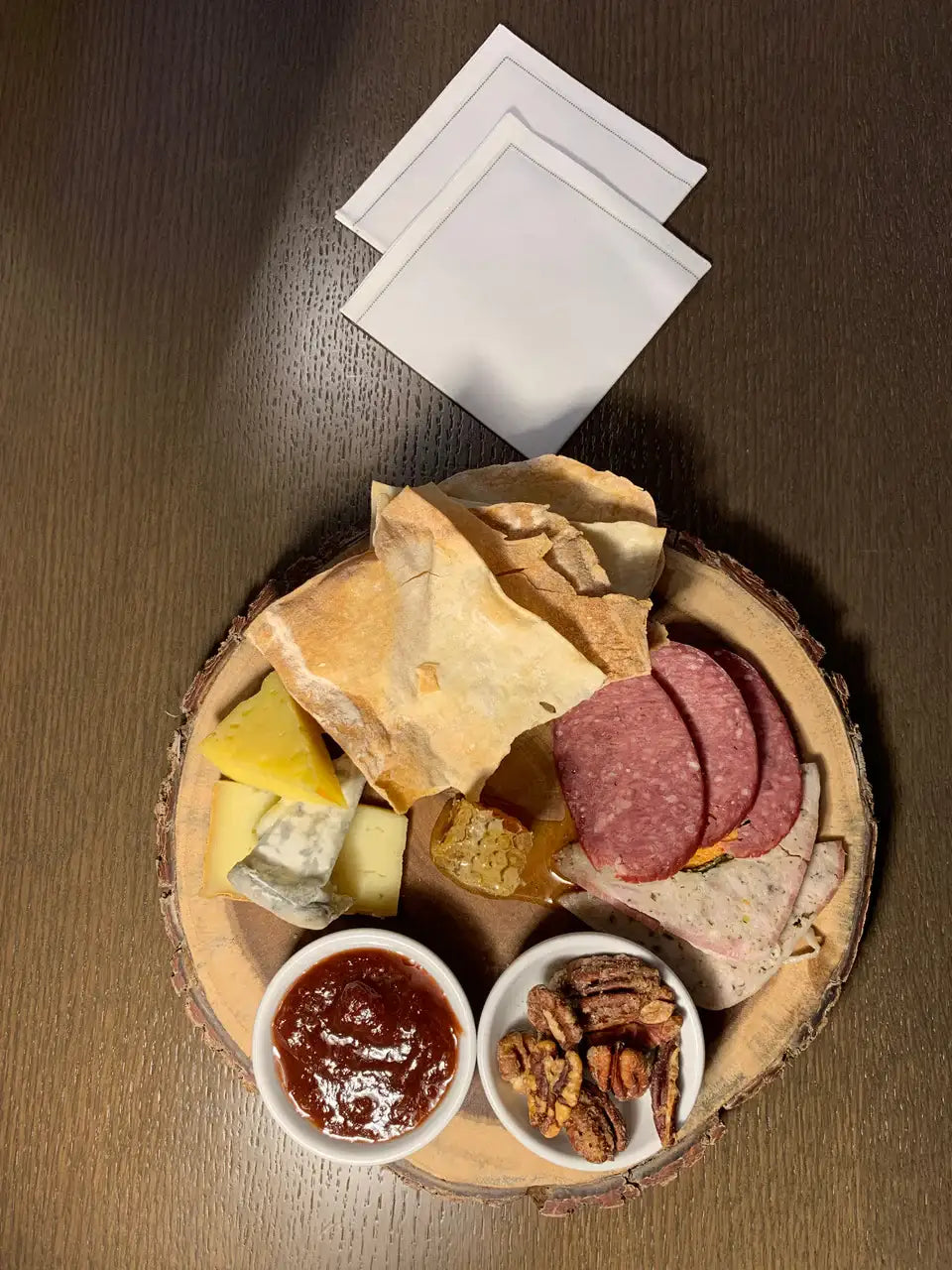 Three white folded organic cotton napkins beside a charcuterie board on a dark table